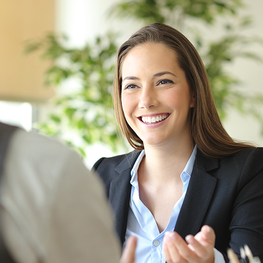 Happy executive coworkers laughing and talking sitting on a desk at the office